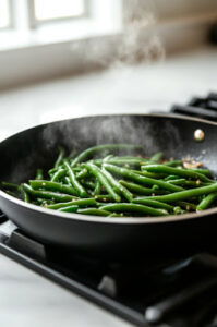 This image shows green beans being stirred in the skillet, fully coated in the bubbling sauce.