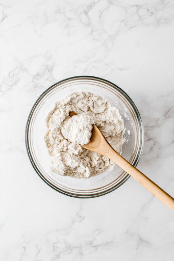 This image shows flour, baking powder, baking soda, and salt being added into the wet ingredients and mixed until the dough forms.