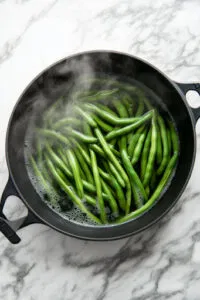 This image shows green beans being cooked until tender but still firm enough to be easily pierced with a fork, ensuring they remain slightly undercooked for further cooking later.