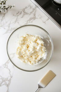 This image shows a person creaming butter and sugar together in a bowl until light and fluffy, forming the base of the cupcake batter.