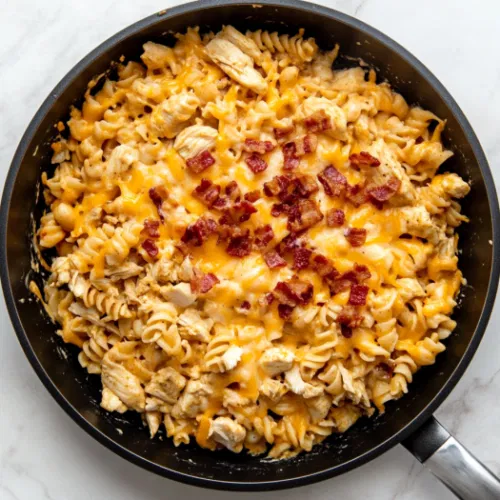 This image shows a bowl of creamy chicken bacon ranch pasta garnished with crispy bacon pieces and shredded cheese, served warm and ready to eat