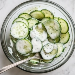 Top-down view of the chilled cucumber salad being served with a slotted spoon, showing the creamy dressing clinging to the cucumber slices.