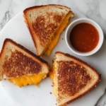 This image shows golden, crispy mini baked grilled cheese sandwiches cut into quarters and served with a side of dipping sauce, ready to enjoy.