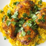 This image shows a plate of grilled curry chicken served over vibrant yellow turmeric rice, garnished with fresh cilantro and accompanied by garbanzo beans.