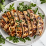 This image shows perfectly grilled Italian chicken breasts garnished with fresh herbs and lemon slices, served on a rustic plate, ready to enjoy.