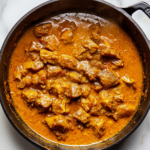 Top-down view of the finished jackfruit curry, garnished with chopped cilantro, served in a bowl on a white marble cooktop background. The dish is vibrant, showcasing tender jackfruit, potatoes, and kale in a rich coconut curry sauce.