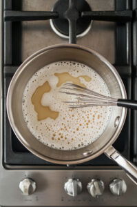 This image shows a medium saucepan with sugar, water, and corn syrup being heated over medium-high heat, as the ingredients dissolve and form a syrup.