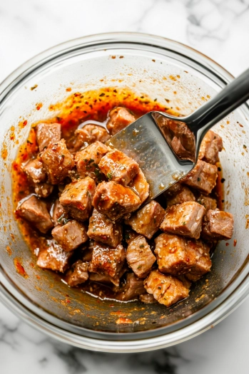 This image shows cubed pork in a bowl being coated with the blended al pastor sauce, ready to be covered and marinated in the refrigerator.