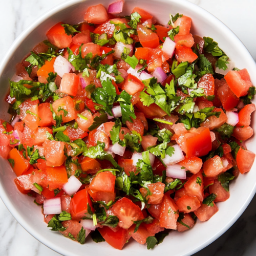 Top-down view of the freshly prepared salsa in a serving bowl on a white marble cooktop. The colorful mix of tomatoes, cilantro, and onions is garnished with extra cilantro, ready to serve.