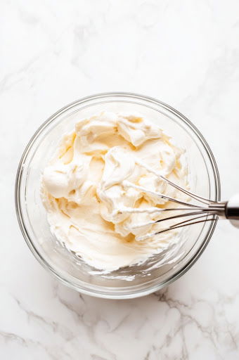 This image shows an electric mixer blending cream cheese and marshmallow crème in a medium bowl until the mixture becomes fluffy and smooth.