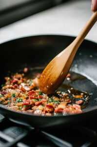 This image shows brown sugar, Dijon mustard, and garlic being added to the skillet with the cooked bacon, stirring until the sauce is well combined.