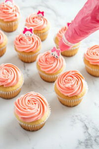 This image shows pink icing being piped onto the cooled cupcakes