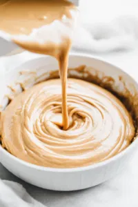 Top-down view of a greased 10-inch Bundt pan as the banana nut batter is poured and evenly spread. The scene captures the smooth, thick batter filling the pan, ensuring even distribution for baking.