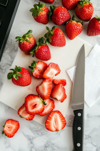 This image shows a person using a paring knife to slice off the tops of each strawberry, making them ready for filling.