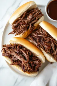 This image shows the finished BBQ beef being served warm on sandwich buns or sliders, ready to enjoy.