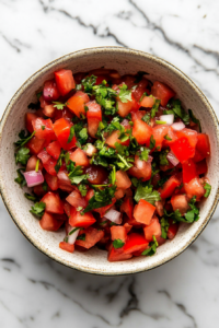 Top-down view of the freshly prepared salsa in a serving bowl on a white marble cooktop. The colorful mix of tomatoes, cilantro, and onions is garnished with extra cilantro, ready to serve.