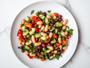 A top-down view of a serving of bean and cucumber salad on a clean white plate on a white marble cooktop. The colorful mixture of beans, cucumber, capers, and parsley is coated with the tangy dressing, ready to be enjoyed.