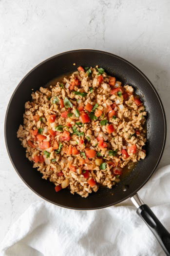 A top-down view of the skillet as chicken broth is added to the seasoned turkey mixture. The broth simmers and thickens slightly, blending with the spices to create a rich, flavorful turkey filling, perfect for the burrito bowls.