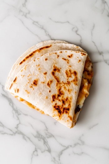 This image shows a quesadilla being sliced into wedges and served warm, with melted cheese and flavorful pork peeking out from the edges.