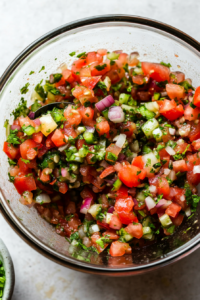 Top-down view of the bowl as the salsa ingredients are well-mixed with a spoon, ensuring even distribution of flavors. Additional salt or lime juice is being adjusted to taste.