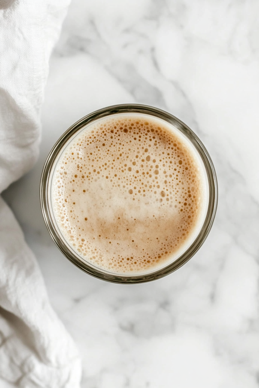 Top-down view of a sealed airtight container or glass bottle filled with homemade Irish cream, placed on a white marble cooktop. The Irish cream is ready to be stored in the refrigerator for up to 2 months.