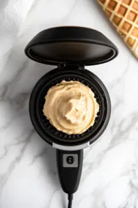 This image shows 2 tablespoons of batter placed in the center of the preheated waffle cone maker, with the lid being closed and locked.