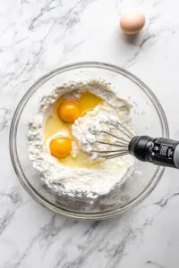 This image shows a large bowl filled with ingredients being mixed on medium speed to create a smooth cupcake batter.