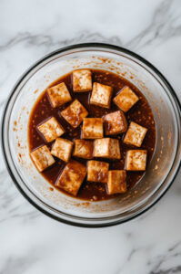 This image shows baked tofu cubes being marinated in sauce for 5 minutes, with occasional stirring.