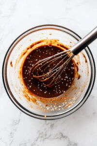 This image shows sauce ingredients being whisked together in a bowl, with the cook adjusting flavors to taste.