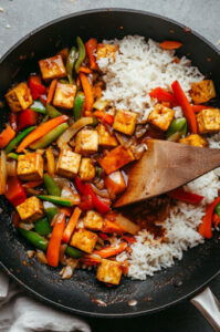 This image shows the cooked tofu and vegetables being served with optional toppings like sriracha or roasted peanuts.