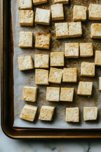 This image shows tofu being diced into cubes and spread evenly on a baking sheet