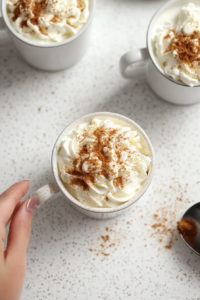 Top-down view of the two mugs with coffee as a generous dollop of whipped cream is spooned on top of each. The soft, creamy layer of whipped cream contrasts with the dark coffee below.