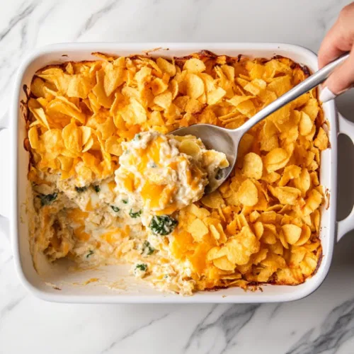 Top-down view of the tuna casserole in the oven, where the potato chips are turning golden brown, and the edges of the casserole are bubbling.