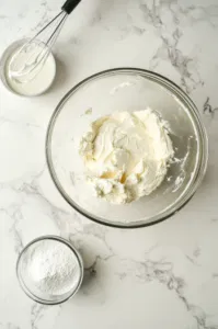 This image shows a bowl of softened cream cheese being whipped with vanilla and powdered sugar to make the smooth cream cheese filling for the donuts.]