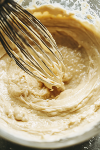 Top-down view of the small mixing bowl as boiling water is poured into the batter, with a whisk blending the ingredients until smooth. The batter is silky and lump-free, ready for the next step.