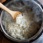 A top-down view of the cooked jasmine rice inside the Instant Pot. A fork is being used to gently fluff the rice, showcasing the tender, perfectly cooked grains ready for serving.