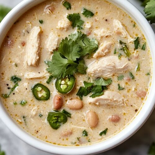 Serving the White Chicken Chili" Alt Text: "A top-down view of a bowl of white chicken chili, garnished with fresh cilantro. The creamy chili is filled with chunks of meat, beans, and jalapeños, making it a warm, comforting dish, ready to be enjoyed