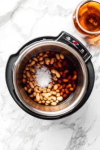 Top-down view of peanuts, water, salt, and liquid smoke being added to the Instant Pot. The ingredients are being stirred before sealing the lid.