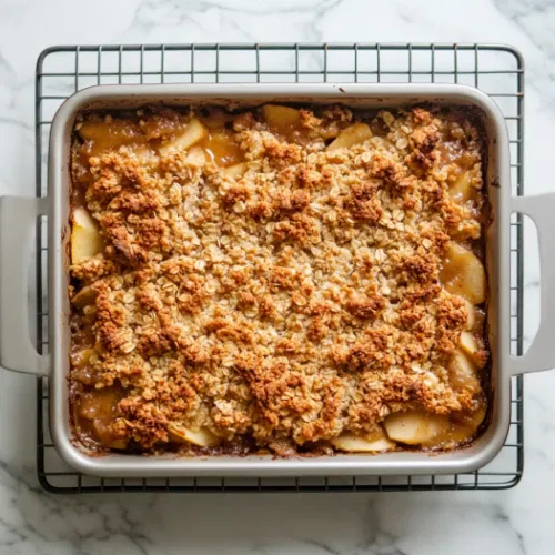 Top-down view of the golden-brown apple crisp fresh out of the oven, cooling on a wire rack with bubbling edges and a crispy oat topping.