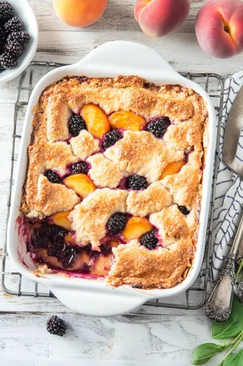 Top-down view of the finished peach and blackberry cobbler, golden brown and bubbly, cooling on a rack after being freshly baked.