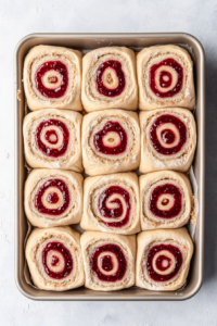 Top-down view of sliced peanut butter and jelly rolls being placed into a greased baking pan, showing the swirl of filling inside each roll.