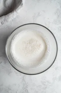 Top-down view of egg whites at the stiff peak stage in the mixer bowl, showing the shiny and thick meringue mixture.