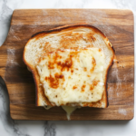 Top-down view of a fully toasted sandwich on a wooden cutting board.