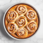 Top-down view of peanut butter and jelly rolls in a pan, with a vanilla glaze being drizzled over the slightly cooled rolls, creating a glossy finish.