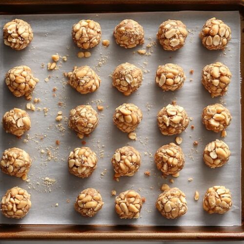 Top-down view of a baking sheet with peanut clusters in the refrigerator. The clusters are setting and hardening, chilling for 30 to 45 minutes to become firm and ready to serve.