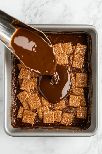 Top-down view of the hot toffee mixture being carefully poured over the graham crackers in the baking pan, spreading it out evenly.