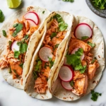 Top-down view of the assembled salmon tacos garnished with fresh cilantro, sliced radishes, and lime wedges, ready to be served.