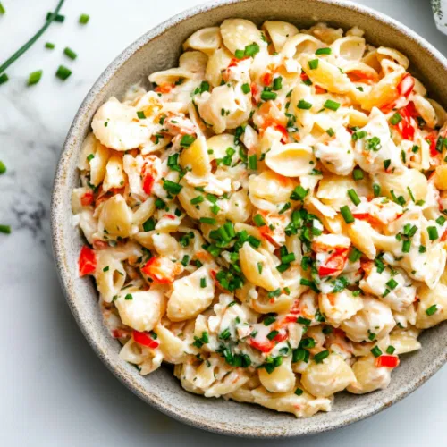 Top-down view of crab pasta salad garnished with freshly chopped chives, served in a large bowl on a white marble surface, ready to be enjoyed