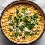 Top-down view of the warm Mexican street corn dip served in a bowl, garnished with extra cotija cheese and cilantro. The creamy, colorful dip is ready to be enjoyed, highlighting the fresh toppings.