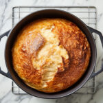 this image shows baked no knead bread in a dutch oven